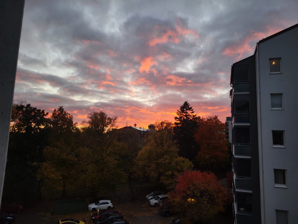 Vuurrode lucht bij zonsondergang boven herfstbomen, gezien vanuit een raam