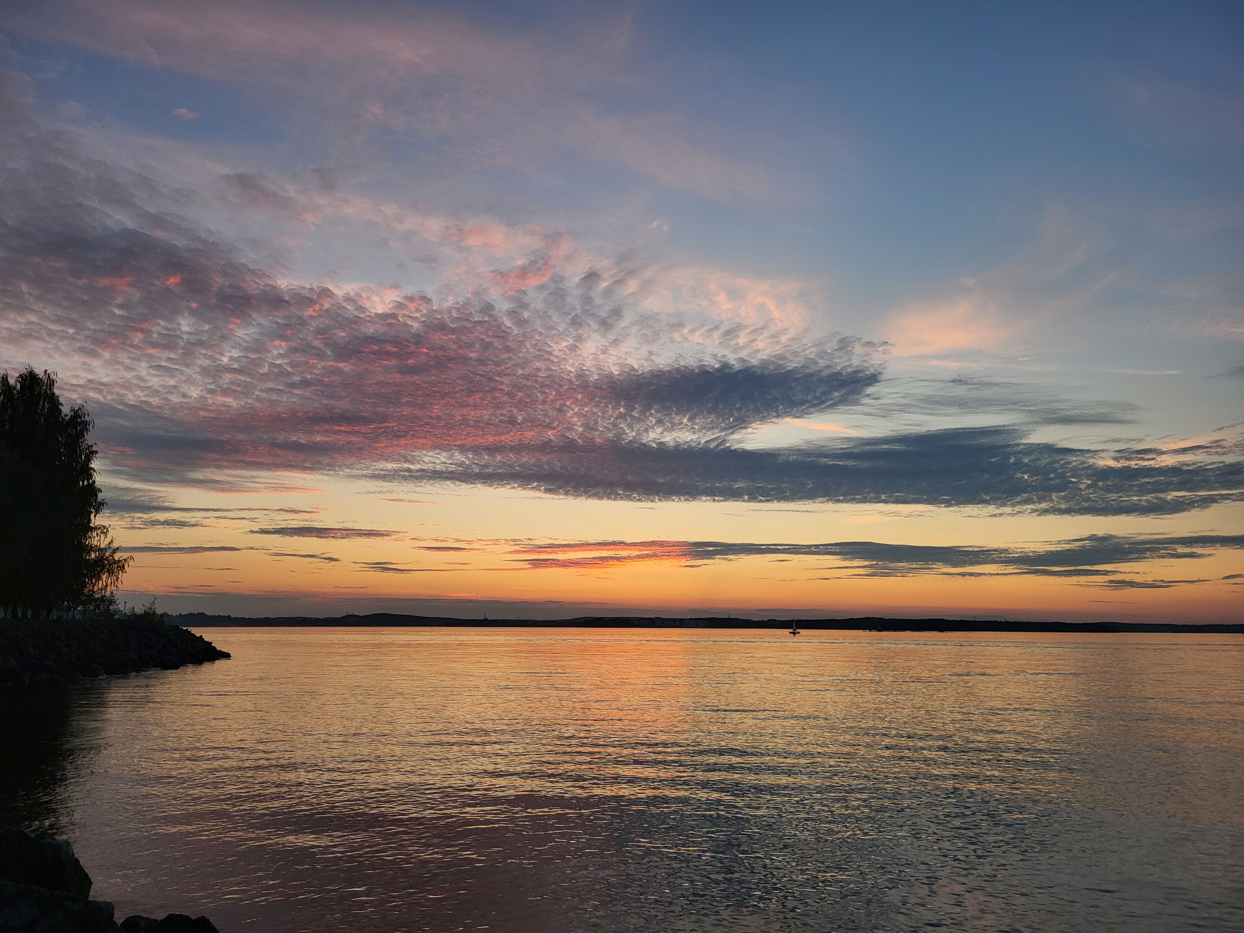 Felroze wolken bij zonsondergang boven een Fins meer met rotsen op de voorgrond, dramatisch en intens